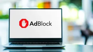 Na szklanym blacie stoi uruchomiony laptop. Na jego ekranie wyświetlane jest logo AdBlock, czyli popularnego w sieci i skutecznego blokera reklam.