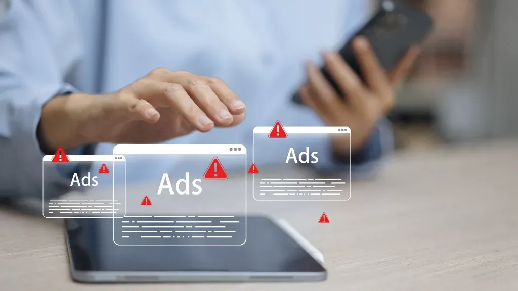 Mężczyzna wyciąga dłoń w stronę leżącego tableta. Nad urządzeniem wyświetla się interfejs, który odwzorowuje wyskakujące okienka reklamowe w sieci.